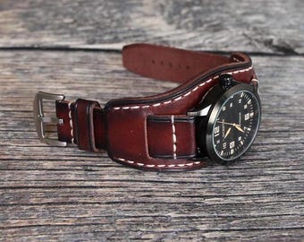 May include: A brown leather watch strap with white stitching. The strap is attached to a black watch with a round face and silver hands. The watch face has the words "OCCHIALI" and "Automatic" printed on it.