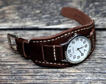 May include: A brown leather watch band with white stitching wraps around a silver watch with a white face and black numbers. The watch face says "Classic Quartz".