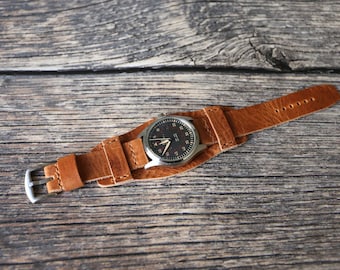 May include: A brown leather watch strap with a silver watch face. The watch face has black numbers and hands.