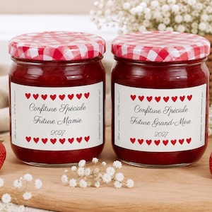 Peut inclure: Deux pots en verre remplis de confiture rouge, chacun surmonté d'un couvercle à carreaux rouges et blancs. Les étiquettes blanches présentent des bordures de cœurs rouges et le texte Confiture Spéciale Future Mamie 2027 et Future Grand-Mère 2027.