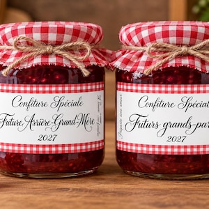 Peut inclure: Deux bocaux en verre remplis de confiture de framboise rouge, surmontés de couvercles en tissu à carreaux rouges et blancs noués avec de la ficelle. Les étiquettes portent le texte Confiture Spéciale, Future Arrière-Grand-Mère 2027 et Futurs grands-parents 2027.