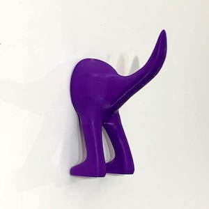 May include: Purple plastic dog hook for hanging items on a wall. The hook is shaped like a dog's hind legs and tail.