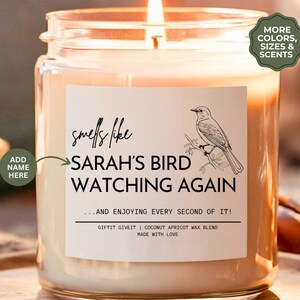 May include: A clear glass candle jar with a white label that reads "smells like SARAH'S BIRD WATCHING AGAIN... AND ENJOYING EVERY SECOND OF IT! GIFTIT GIVEIT | COCONUT APRICOT WAX BLEND MADE WITH LOVE". The label also features a black and white illustration of a bird perched on a branch.