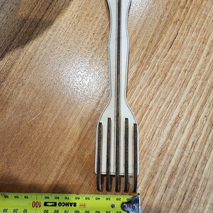 K&ouml;nnte beinhalten: Eine Holzgabel mit braunem Griff und f&uuml;nf Zinken. Die Gabel ist 43 cm lang und wird mit einem gelben Ma&szlig;band gemessen.