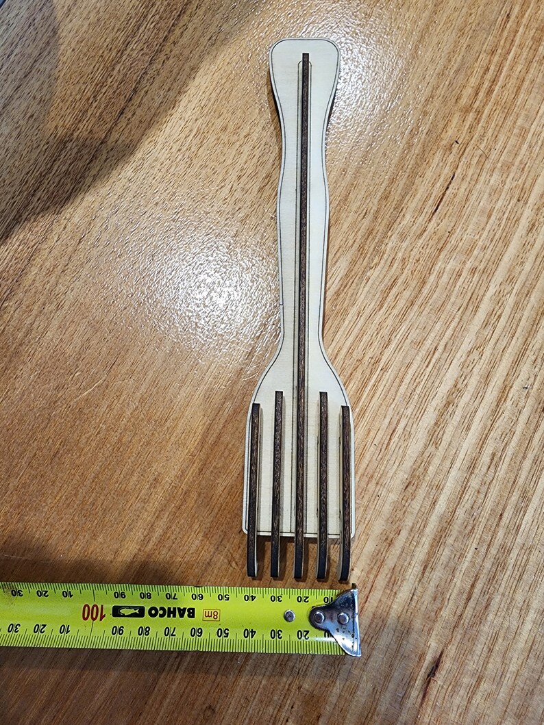 K&ouml;nnte beinhalten: Eine Holzgabel mit braunem Griff und f&uuml;nf Zinken. Die Gabel ist 43 cm lang und wird mit einem gelben Ma&szlig;band gemessen.