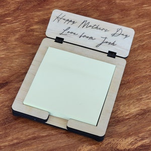 May include: A wooden notepad holder with a message that reads "Happy Mothers Day Love from Josh". The holder has a slot for a notepad and a black elastic band to hold the notepad in place.