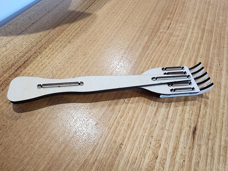 K&ouml;nnte beinhalten: Eine Holzgabel mit einem langen Stiel und f&uuml;nf Zinken. Die Gabel ist aus hellbraunem Holz und hat eine nat&uuml;rliche Oberfl&auml;che.