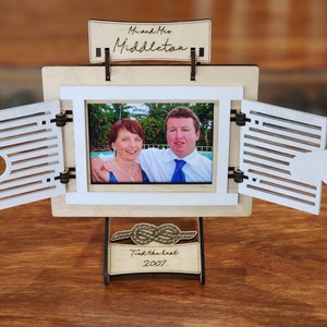 May include: A wooden photo frame with a white shutter design. The frame is open to reveal a photo of a couple. The frame has a stand with a rope knot design and the text "Tied the knot 2007".