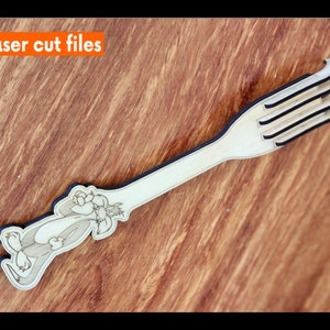 Può includere: Un gratta schiena in legno con un design di personaggio dei cartoni animati e una superficie di grattamento a quattro punte. "Laser cut files" è scritto in arancione nella parte superiore dell'immagine.
