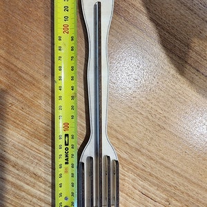 K&ouml;nnte beinhalten: Eine Gabel aus Holz mit einem braunen Griff und f&uuml;nf Zinken. Die Gabel wird mit einem gelben Ma&szlig;band gemessen.