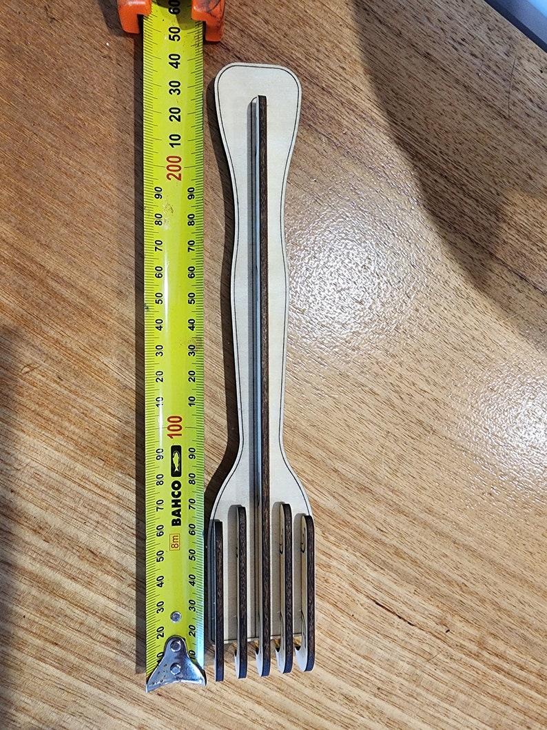 K&ouml;nnte beinhalten: Eine Gabel aus Holz mit einem braunen Griff und f&uuml;nf Zinken. Die Gabel wird mit einem gelben Ma&szlig;band gemessen.