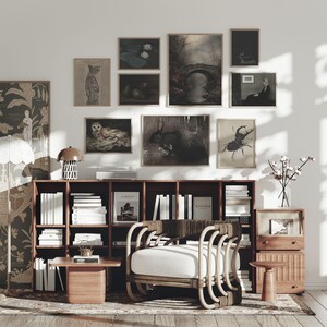 May include: A cozy living room scene featuring a wooden bookshelf filled with books, a rattan chair with a white cushion, and a small wooden side table. The wall is adorned with framed vintage art prints, including botanical and animal illustrations, creating a warm, inviting atmosphere.
