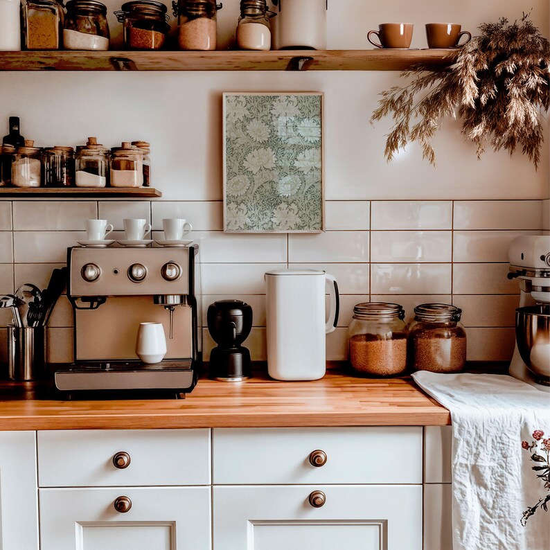 May include: A white kitchen with a coffee maker, a white water pitcher, and two glass jars filled with brown sugar. The kitchen has white cabinets and a wooden countertop. There is a framed print on the wall above the coffee maker.