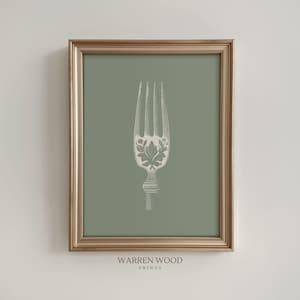 May include: A framed print featuring a detailed illustration of a fork in white against a muted green background. The fork has an ornate design on the handle and tines. The frame is gold, and the text "WARREN WOOD PRINTS" is at the bottom.
