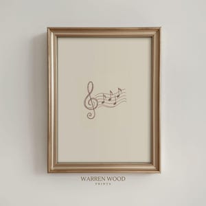 May include: A framed print with a musical treble clef and notes in brown. The artwork is set against a cream background and framed in a gold-toned frame. The text "WARREN WOOD PRINTS" is printed at the bottom of the print.