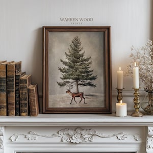 May include: Framed print featuring a winter scene with a tall evergreen tree and a deer. The artwork is in a dark brown wooden frame. The text "WARREN WOOD PRINTS" is at the top. The scene is set on a white mantel with candles and books.