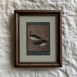 May include: Framed art print featuring two geese with black and white plumage, set against a brown backdrop with a decorative border. The dark brown frame complements the artwork. The text "WARREN WOOD PRINTS" is at the bottom.
