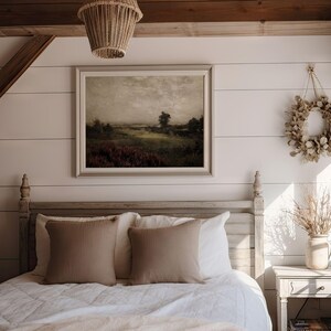 May include: A bedroom scene featuring a framed landscape painting, a bed with tan pillows, and a decorative wreath. The painting depicts a field with trees under a cloudy sky. A woven light fixture hangs from the ceiling.