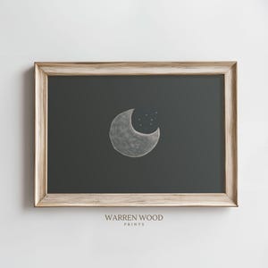 May include: A framed print of a crescent moon with stars on a dark background. The frame is a light wood color. The print is titled "WARREN WOOD PRINTS".