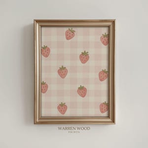 May include: A framed print with a repeating pattern of pink strawberries on a light pink and white gingham background. The print is in a gold-coloured frame. The text "WARREN WOOD PRINTS" is at the bottom.