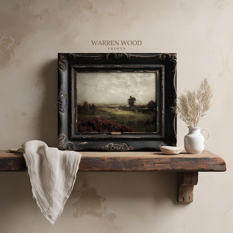 May include: A framed landscape print with a black ornate frame. The print depicts a field with red flowers and a tree under a cloudy sky. The text "WARREN WOOD PRINTS" is visible at the top. The print is displayed on a wooden shelf.