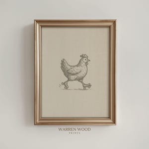 Op de afbeelding: Ingelijste print met een grillige illustratie van een kip op rolschaatsen. Het kunstwerk is in vintage stijl, met een neutraal kleurenpalet. De lijst is goudkleurig en de print bevat de tekst "WARREN WOOD PRINTS" aan de onderkant.