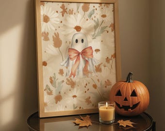 May include: A framed print featuring a ghost with a bow, set against a floral background. A carved pumpkin, a lit candle in a glass, and autumn leaves are on a table. The artwork and decor create a Halloween theme.