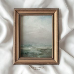 May include: A framed landscape print with a muted color palette. The artwork depicts a seascape with a cloudy sky and water in shades of gray and green. The frame is made of wood with a warm brown finish. The text "WARREN WOOD PRINTS" is printed at the bottom.