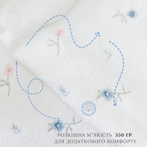 May include: White organic cotton towel with embroidered flowers in blue and pink. The towel is 550 grams and features a label that says "100% Organic Cotton".