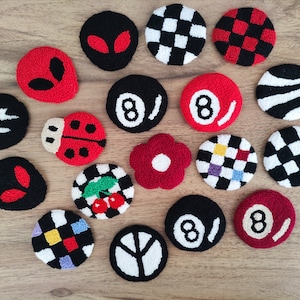 May include: A collection of 16 colorful, round, embroidered patches with various designs, including a ladybug, cherries, a flower, a checkered pattern, and an alien face.