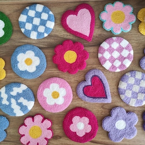 May include: A collection of 15 colorful, round, and heart-shaped coasters with various designs, including flowers, checkered patterns, and hearts. The coasters are made of a soft, plush material and are perfect for protecting surfaces from scratches and spills.