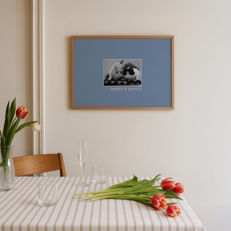 a dining table with a vase of red tulips, a glass of water, and a framed photo of two cats.