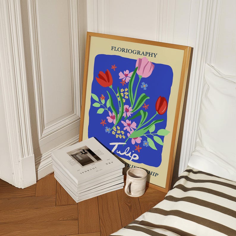 a framed poster of a floral design, a stack of books, and a striped blanket on a wooden floor.