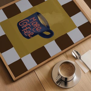 a wooden table with a framed print of a coffee mug and a cup of coffee on it, along with a spoon and a napkin.