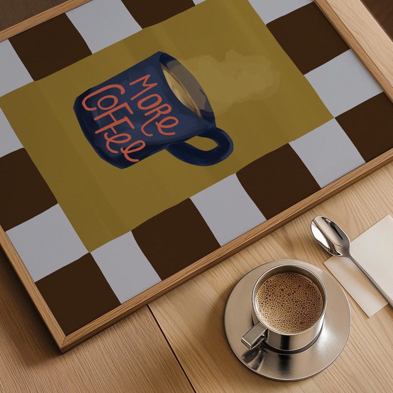 a wooden table with a framed print of a coffee mug and a cup of coffee on it, along with a spoon and a napkin.