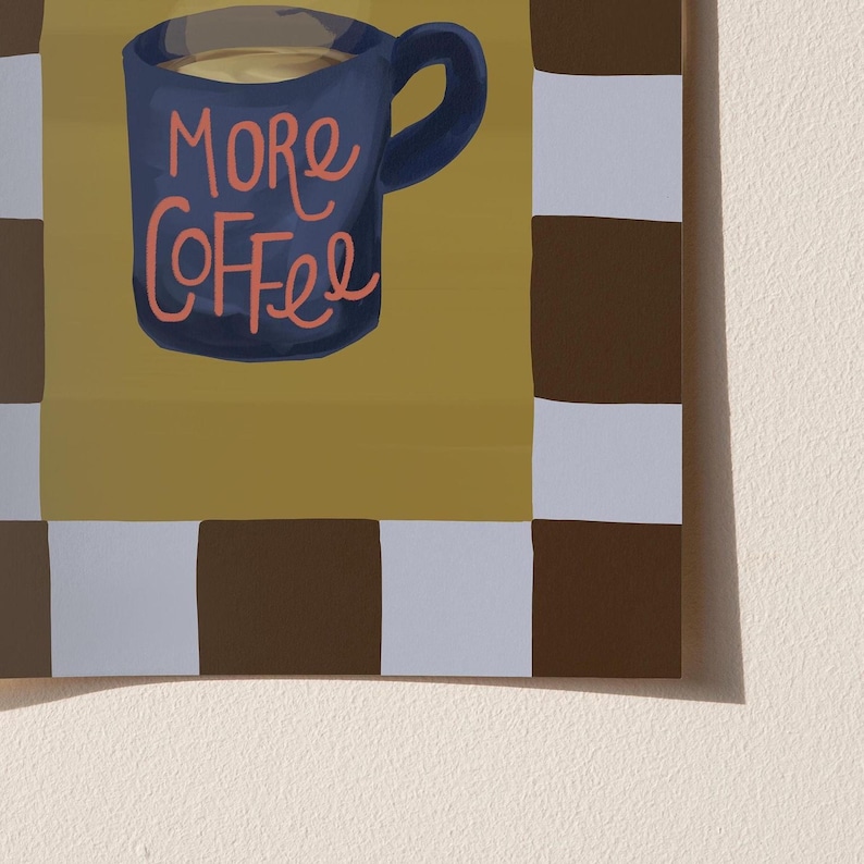 a blue mug with the text "More Coffee" written on it, set against a background of a checkered pattern in shades of brown and white.