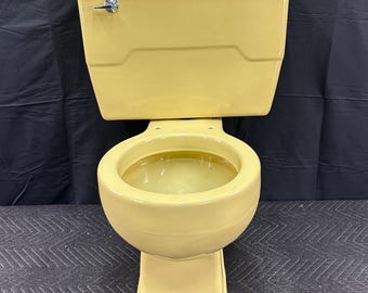 May include: A vintage, yellow toilet with a matching tank and seat. The toilet has a classic design, with a rounded bowl and a rectangular tank. The flush handle is silver. The toilet is made of ceramic and is likely from the mid-20th century.