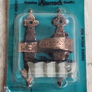 May include: A copper-toned bar latch for flush doors, packaged on a teal card. The latch has a textured finish and is labeled "Amerock Quality". The package also includes the text "A-8550-AC BAR LATCH".