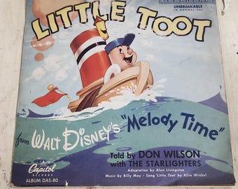Könnte beinhalten: Ein Vintage-Schallplattencover mit einer Cartoon-Illustration eines rot-weiß-blauen Schleppdampfers namens "Little Toot" aus Walt Disneys "Melody Time". Das Album ist eine Capitol Records Superflex Schallplatte, die bei normalem Gebrauch unzerbrechlich ist. Das Album trägt den Titel "Little Toot" und enthält den Text "from Walt Disney's "Melody Time"" und "Told by Don Wilson with The Starlighters".
