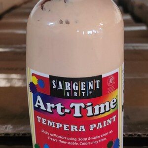 May include: A bottle of Art-Time tempera paint with a peach-colored liquid. The label features the brand name "Sargent Art" and product details. The bottle has a white cap and is designed for art projects.