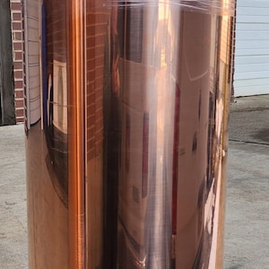 May include: A large roll of copper sheet metal wrapped in clear plastic. The copper has a shiny, reflective surface.