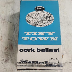May include: A blue box with the text "Ideal Models" and "Tiny Town cork ballast" printed on it. The box features a black and white illustration of a train track winding through a mountain pass. The bottom of the box shows a black and white illustration of a train.