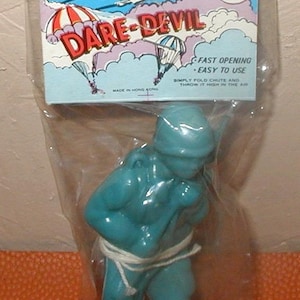 May include: A vintage Dare Devil toy, featuring a blue plastic figure with a parachute, packaged in a clear plastic bag. The packaging has a colorful design with the text "DARE-DEVIL" and instructions. Made in Hong Kong.