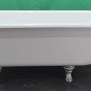 May include: A vintage-style, freestanding bathtub with a white interior and a light gray exterior. The tub has a rounded rim and sits on decorative, claw-foot style legs. The tub's dimensions are approximately 60 inches long.