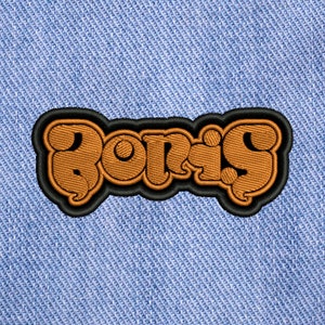 May include: A brown embroidered patch with the word "Boris" in a stylized font. The patch is on a blue denim background.