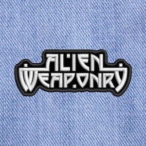 May include: A black and white embroidered patch with the text "ALIEN WEAPONRY" in a stylised font.
