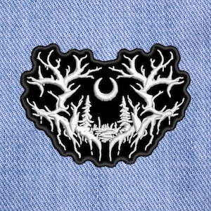 May include: Black embroidered patch with a white design of a crescent moon and two trees with branches reaching up. The design is reminiscent of a forest scene.