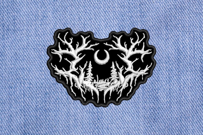 May include: Black embroidered patch with a white design of a crescent moon and two trees with branches reaching up. The design is reminiscent of a forest scene.