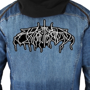 Könnte beinhalten: Eine schwarze Jeansjacke mit einem weißen gestickten Aufnäher auf der Rückseite. Der Aufnäher zeigt ein stilisiertes Design mit dem Wort "Emperor" in Weiß.