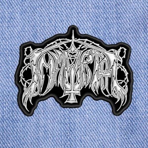 Peut inclure: Écusson brodé avec le mot "IMMORTAL" dans une police gothique, entouré de vignes épineuses. Le patch est noir avec une broderie argentée et un bord noir. Il est présenté sur un fond en denim bleu clair.
